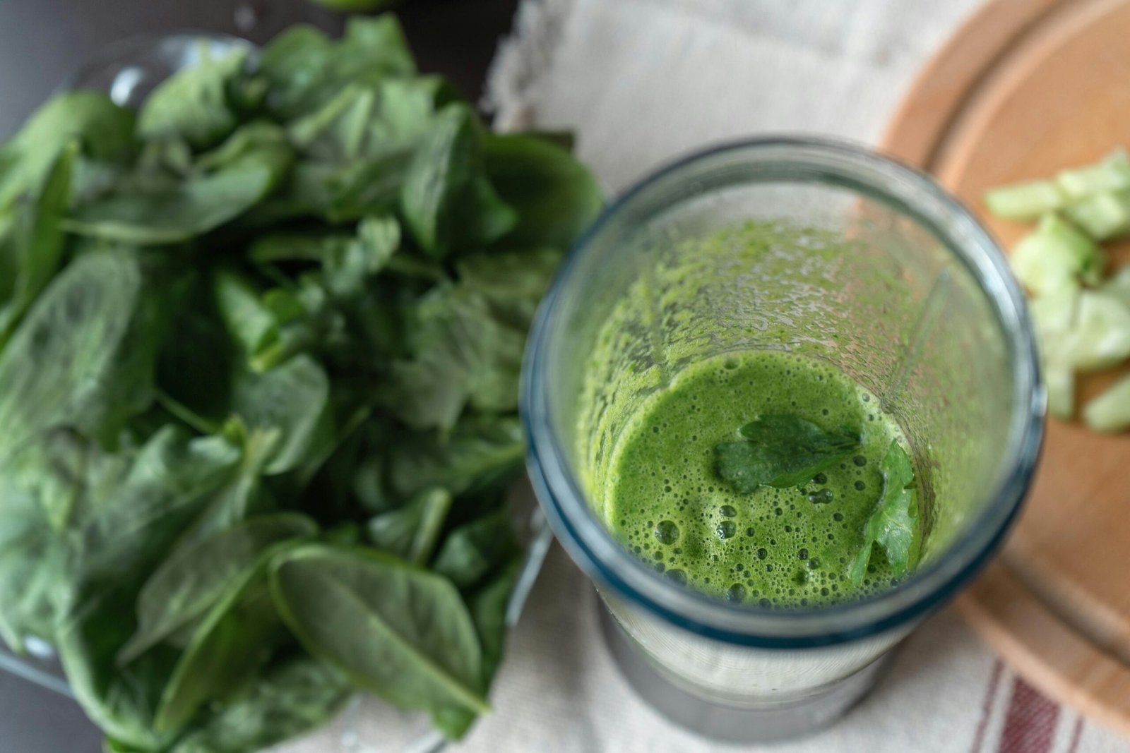 A refreshing green smoothie made with fresh spinach and cucumber on a wooden board.